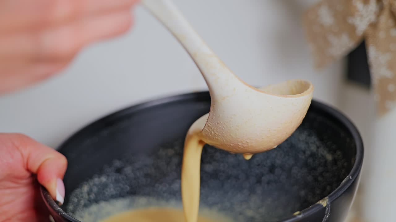 Close-up of pancake batter flowing from ladle in slow motion during prep process