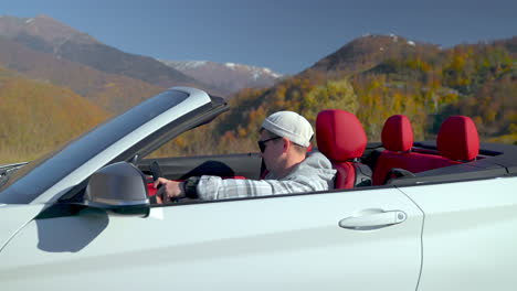 man driving a convertible through scenic mountains in autumn