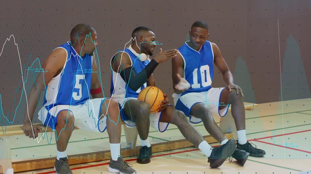 Tres jugadores de baloncesto sentados en el banquillo, el del centro con el balón, liderando la conversación tras la entrada de un compañero.