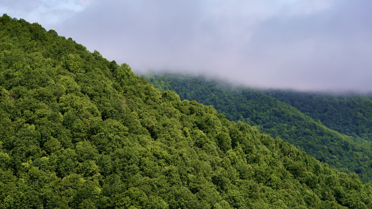 High-altitude drone footage of cloud banks clashing with misty mountain slopes