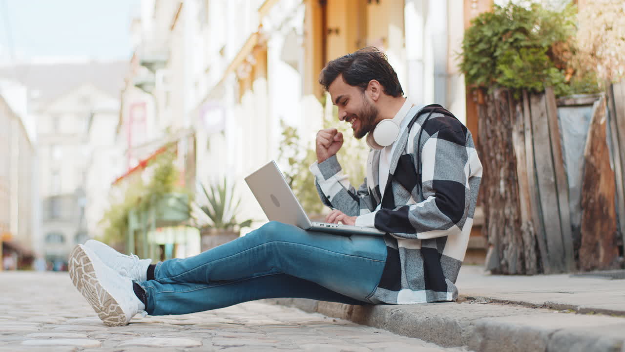 Happy man using laptop celebrating win good message news lottery jackpot victory sitting on street