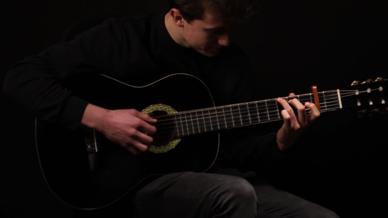 foto de un hombre tocando la guitarra en un estudio con un fondo negro