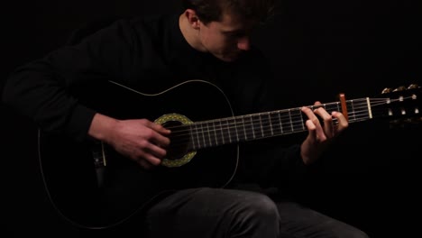 foto de un hombre tocando la guitarra en un estudio con un fondo negro