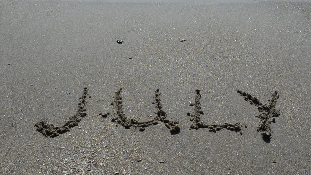 Iscrizione del nome del mese sulla sabbia, la spiaggia. Scatto sulla spiaggia.