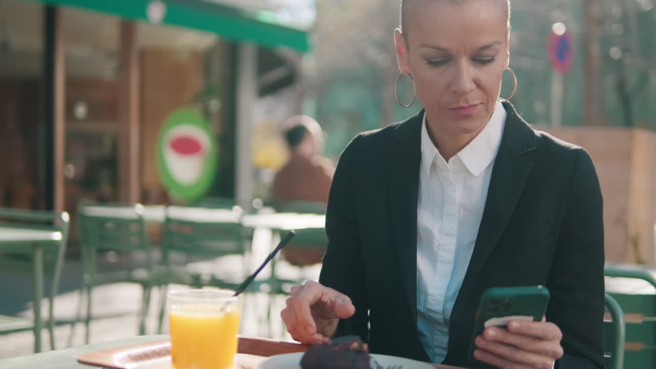 Happy Bald Woman Using Phone and Eating Cake at Outdoor Cafe