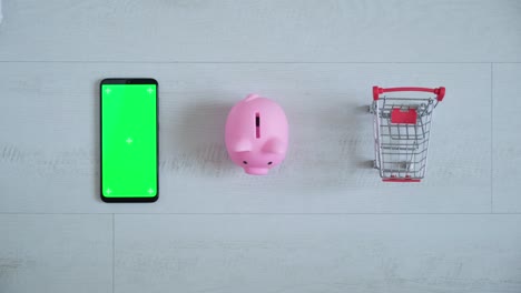 teléfono con una pantalla chromakey en las manos de un primer plano. vista superior de la caja de ahorros del teléfono inteligente y el carrito de compras copia el espacio sobre fondo blanco