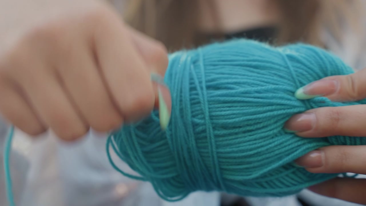Close up of woman holding turquoise yarn preparing to crochet with soft lighting and natural nail polish. focus remains on hands manipulating thick thread emphasizing texture detail