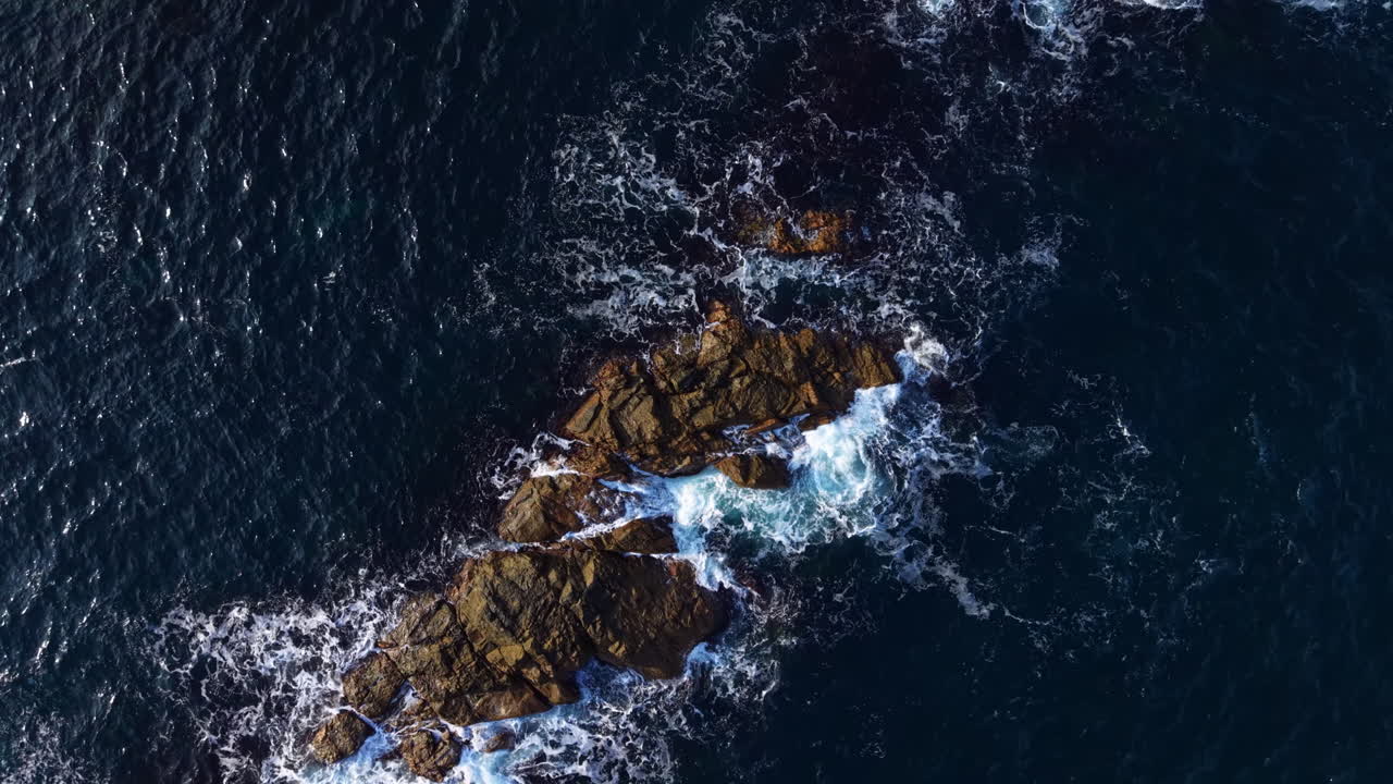 Waves crash over rugged rocks as the sun sets, painting the sky with vibrant colors and reflecting the beauty of nature's coastal wonders