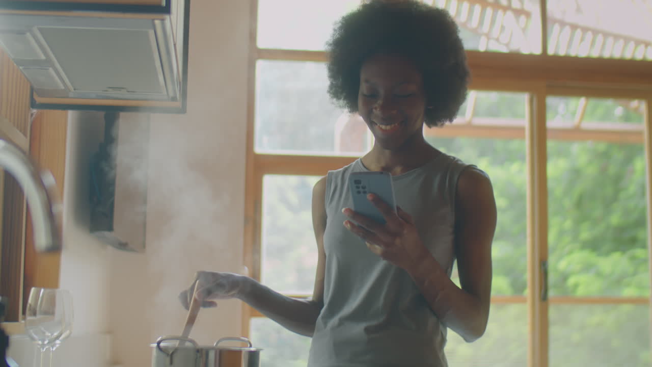 African American Woman Using Phone and Cooking Food