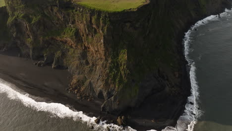 dramatic black sand beach and cliff coastline, aerial view