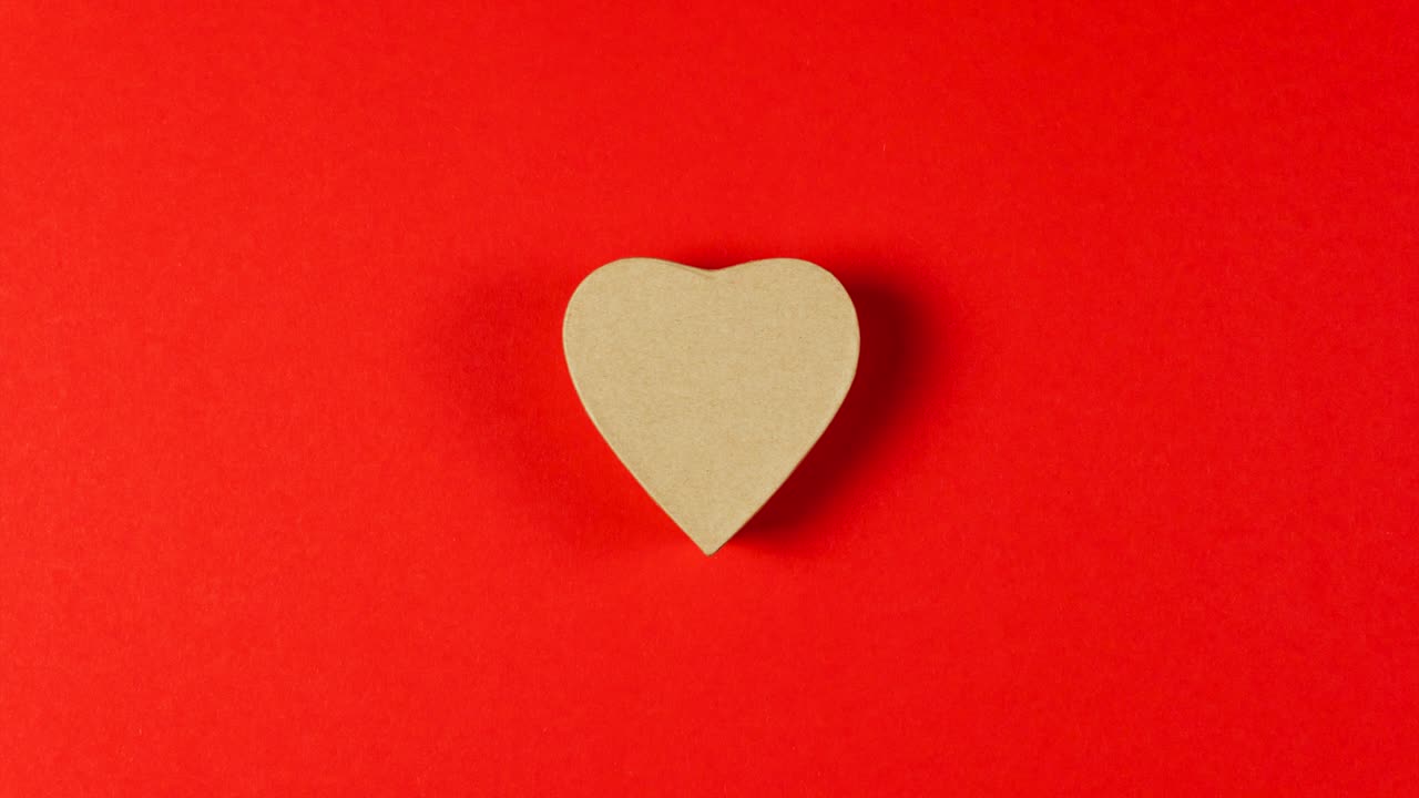 Animazione stop motion. Il cuore rosso e dorato brillante si muove verso una scatola regalo di carta a forma di cuore.