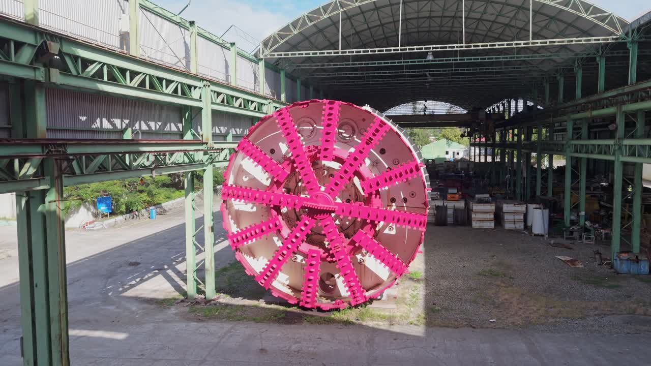 Massive underground tunnel boring machine (TBM) with pink cutting heads, designed for large-scale excavation and tunneling projects, inside an industrial facility