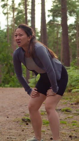 Video-Vertical-De-Una-Mujer-Haciendo-Ejercicio-Al-Aire-Libre-Corriendo-Por-Una-Pista-En-El-Bosque,-Deteniéndose-Para-Tomar-Aire,-Filmado-En-Tiempo-Real-2