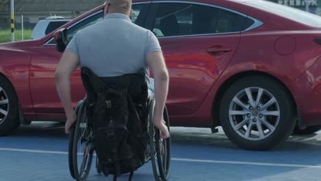 young handicapped driver getting in red car from wheelchair