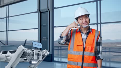 ingeniero asiático con casco de seguridad de pie en una fábrica de alta tecnología, analizando el concepto de la máquina robótica. sonriendo a la cámara y haciendo el gesto de llamarme