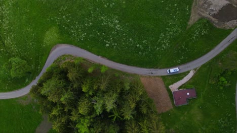 White-camper-van-driving-through-the-winding-mountain-road-around-the-alps---top-view