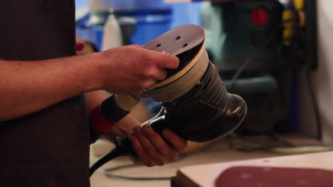 craftsperson putting sandpaper discs on sander device