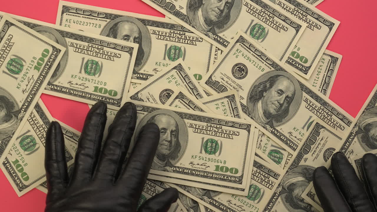 Mani guantate che muovono banconote da cento dollari USA su sfondo rosa
