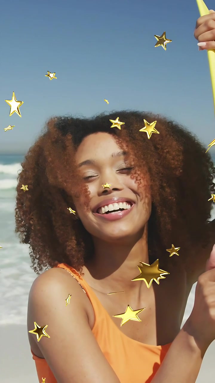 Video verticale: Donna che afferra un palo sulla spiaggia, sorridendo mentre stelle dorate fluttuano sul viso per i creatori.