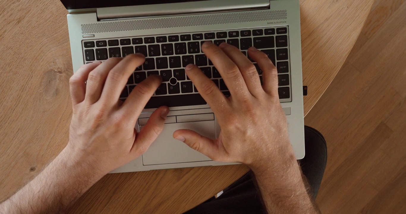 Vista dall'alto di mani che digitano su una tastiera di laptop su una scrivania di legno. Concetto di tecnologia moderna per lavoro a distanza, produttività, comunicazione e uso quotidiano del computer