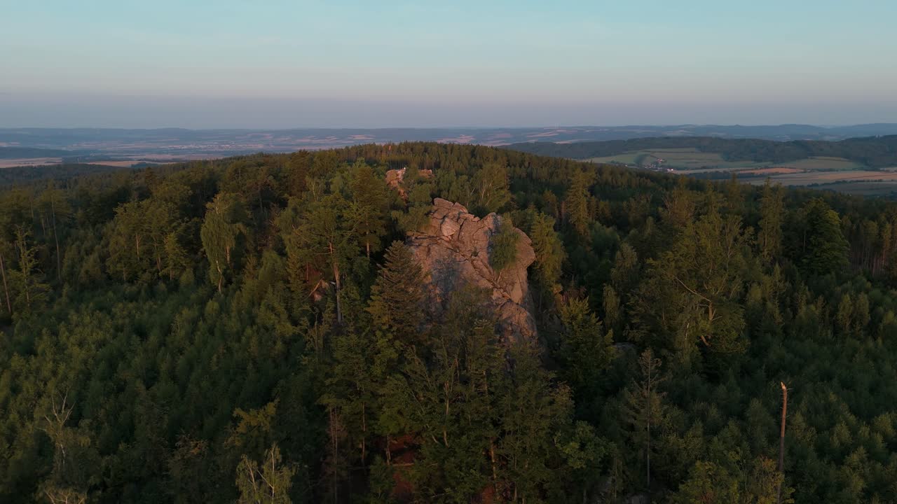 Luftfoto af en klippe, der titter frem fra en skov oplyst af morgensol