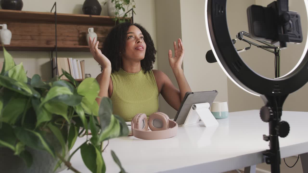 African American adult woman starting camera speaking gesturing in studio touching tablet near mic