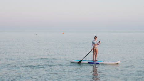 woman paddleboarding in calm water at sunset