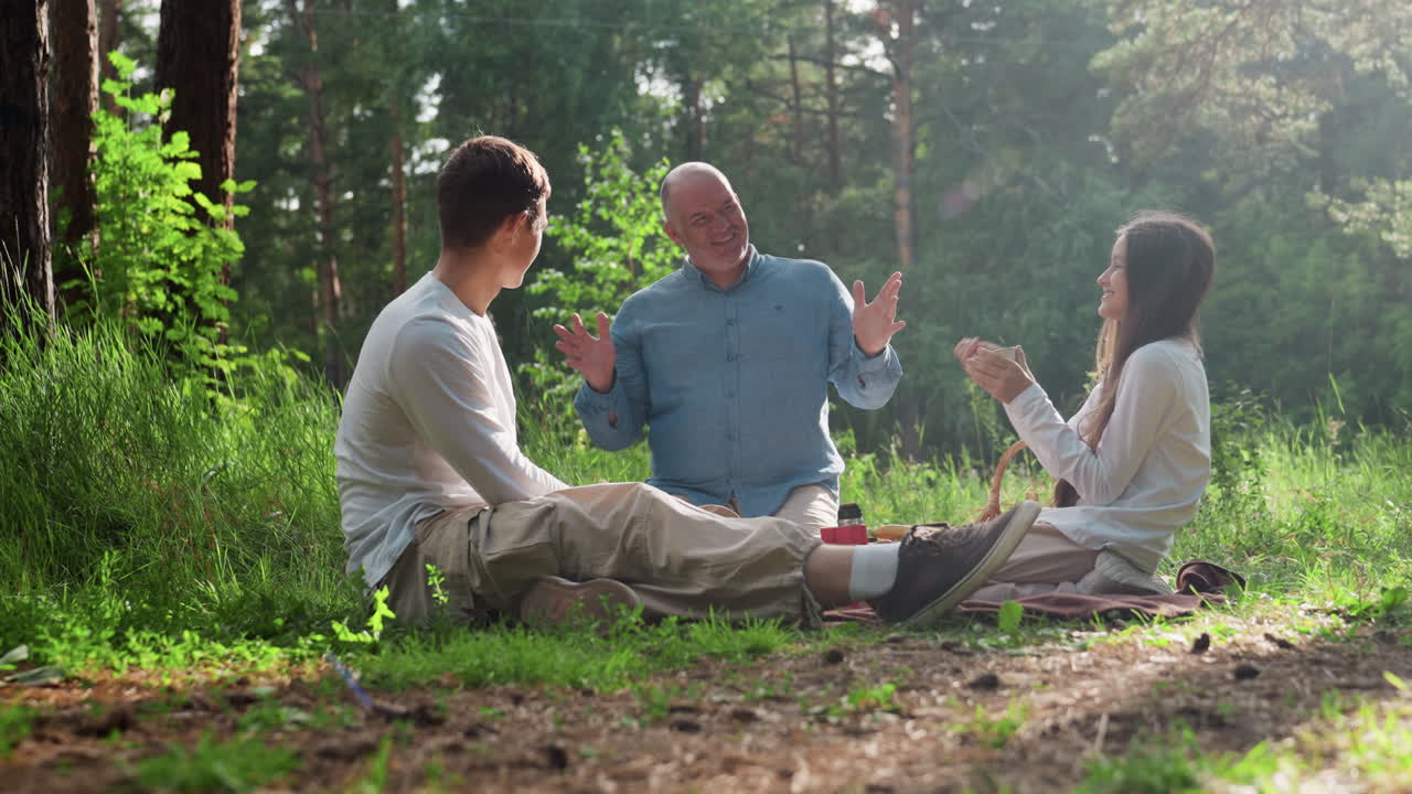 Dad talking with kids during family picnic in green forest, using hands to explain story while children listen with attention, warm sunlight highlighting peaceful bonding and joyful outdoor moment