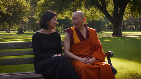 a monk and a woman engaging in conversation on a park bench
