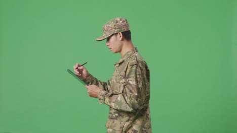 side view of asian man soldier taking note on a tablet while walking in the green screen background studio