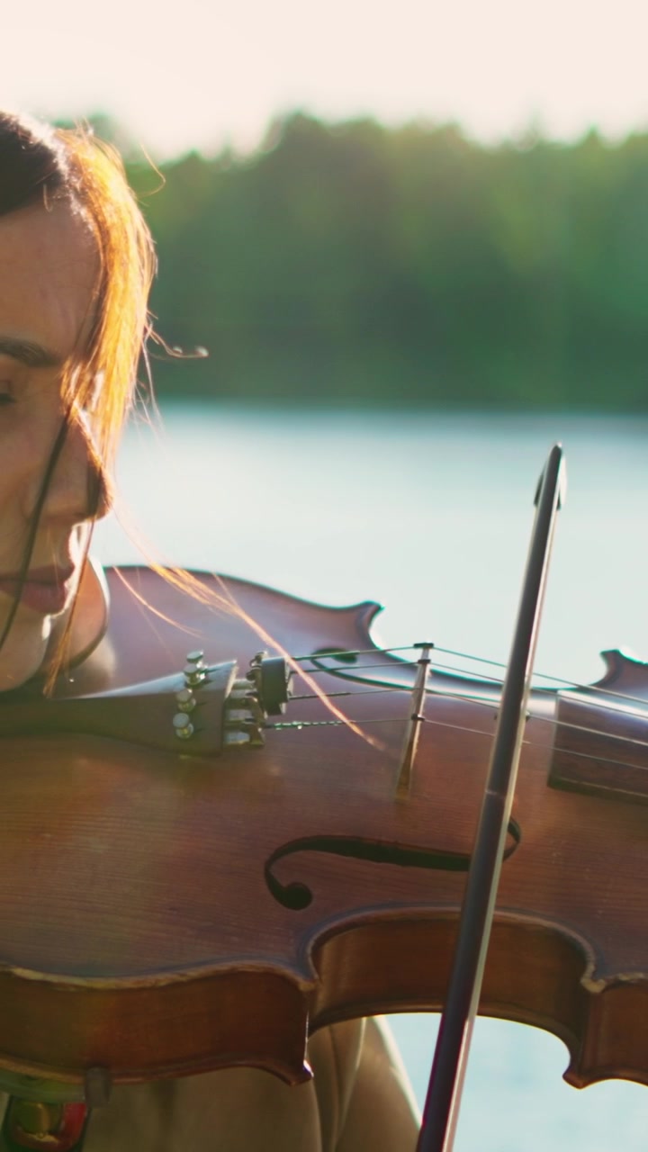 Woman Playing Violin Outdoors by a Lake at Sunset