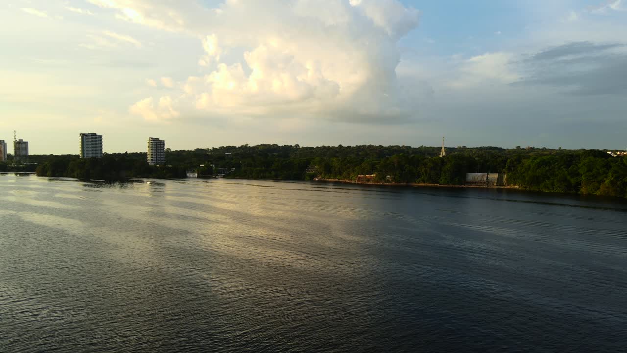 Scena nad wodą w dzielnicy plażowej Ponta Negra w Manaus podczas popołudniowej złotej godziny z częściowo zachmurzonym niebem, Amazonia, Brazylia. Płynne ujęcie z lotu ptaka w 4K z lewej strony.