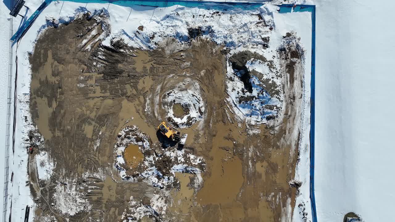 Aerial view of a snowy construction site with an excavator working