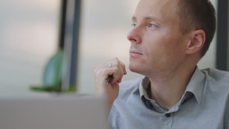 young thoughtful business man thinking of problem solution working on laptop. serious doubtful male professional looking away at laptop considering market risks making difficult decision