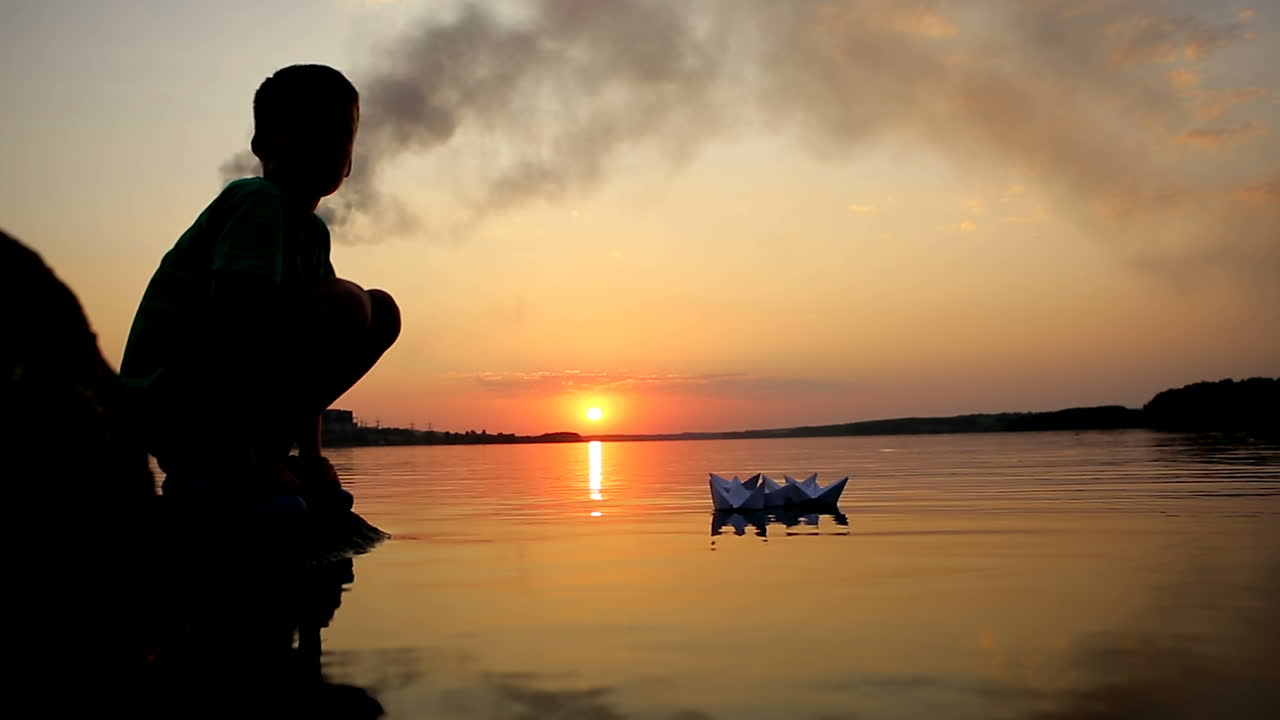 Boy Launching Paper Boat. Little boy launching paper boat on water from beach