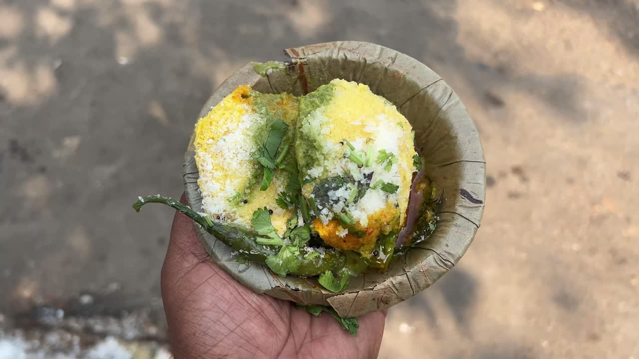 South Indian idli dhokla served with chutney and chilli on disposable plate during daytime.