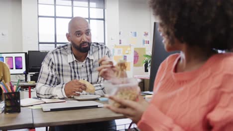 two happy diverse creative colleagues in discussion during lunch in casual office, slow motion