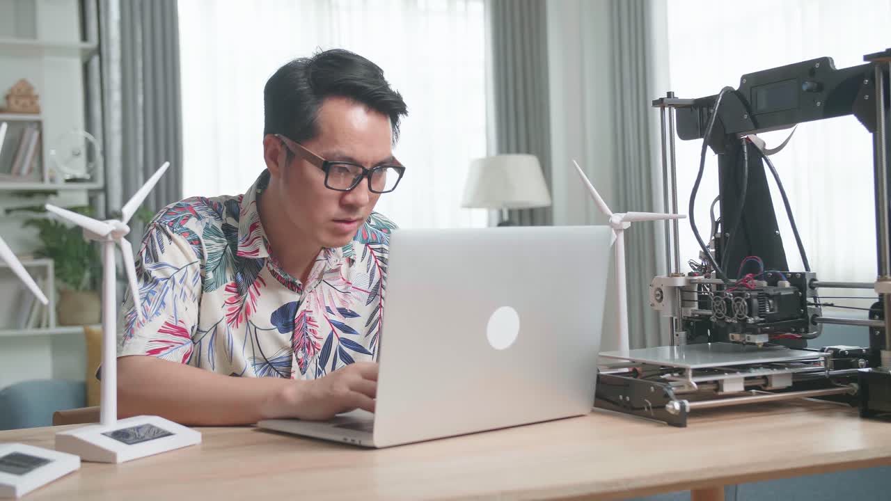 Man using laptop and 3D printer, focusing on renewable energy model