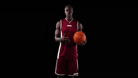 male basketball player holding ball against black background