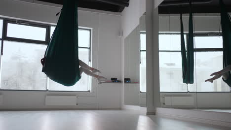young beautiful woman practice in aero stretching swing. young woman rolls her head upside down in a hammock for aerial yoga. focused pretty mature woman doing aerial yoga in gym