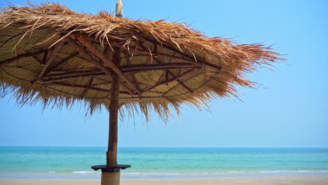 Sombrilla-De-Paja-Hecha-A-Mano-En-La-Playa-Contra-El-Fondo-Del-Océano