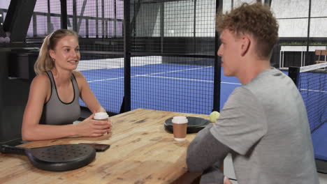 discussing padel strategy, young man and woman enjoying coffee at indoor court table