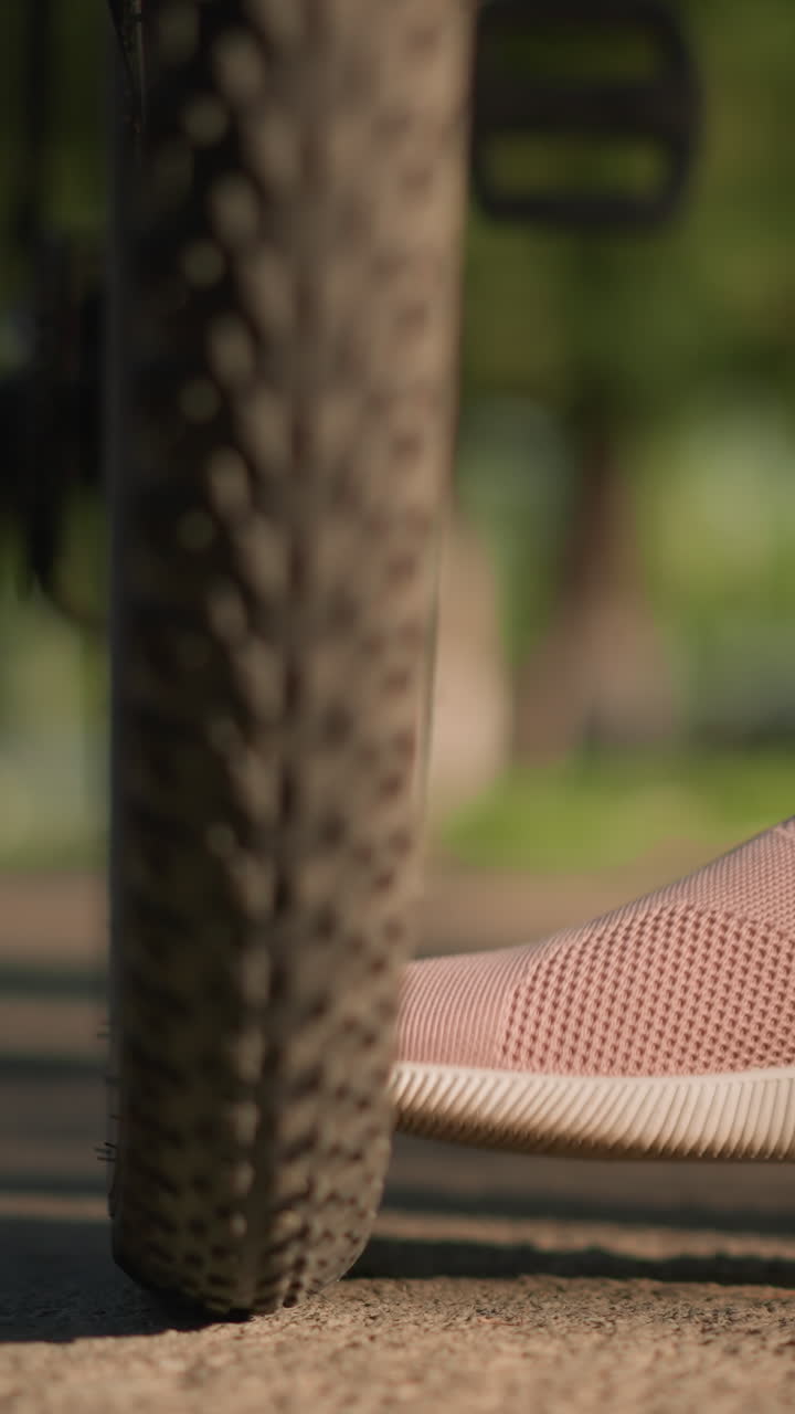 primer plano de piernas con zapatillas rosadas pateando neumáticos de bicicleta para comprobar la presión del aire, vegetación exuberante y árboles borrosos en el fondo