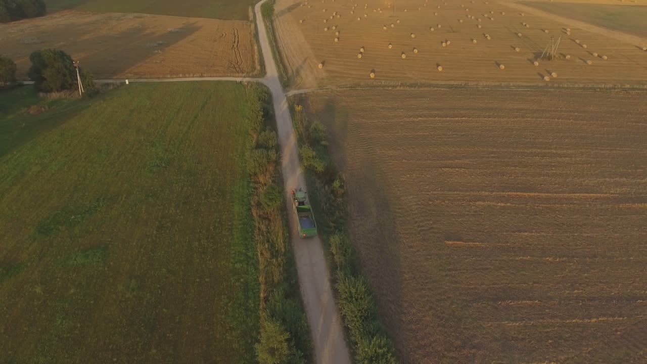 화창한 여름 저녁에 농지를 통과하는 시골 자갈길을 따라 트레일러가 달린 트랙터