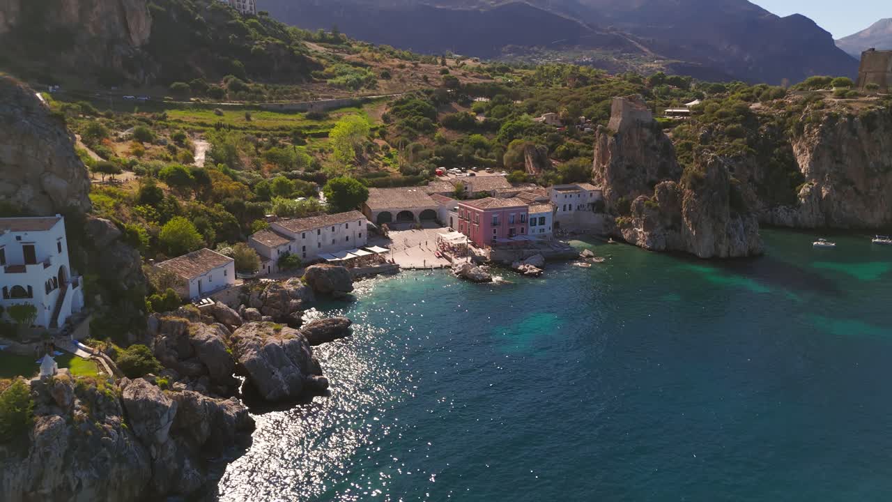 Aerial drone pulling back to reveal Tonnara di Scopello and turquoise Sicilian coast in bright summer light