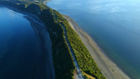 drone circling a road in middle of a steep culmen ridge in sunny chiloe, chile