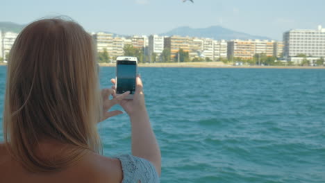 Frau-Mit-Handy-Schießt-Vom-Schiff-Aus-Auf-Meer-Und-Stadt