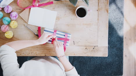 overhead shot looking down on woman at home writing in birthday card and wrapping gift