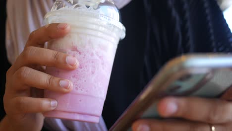 woman holding pink frappe and using mobile phone