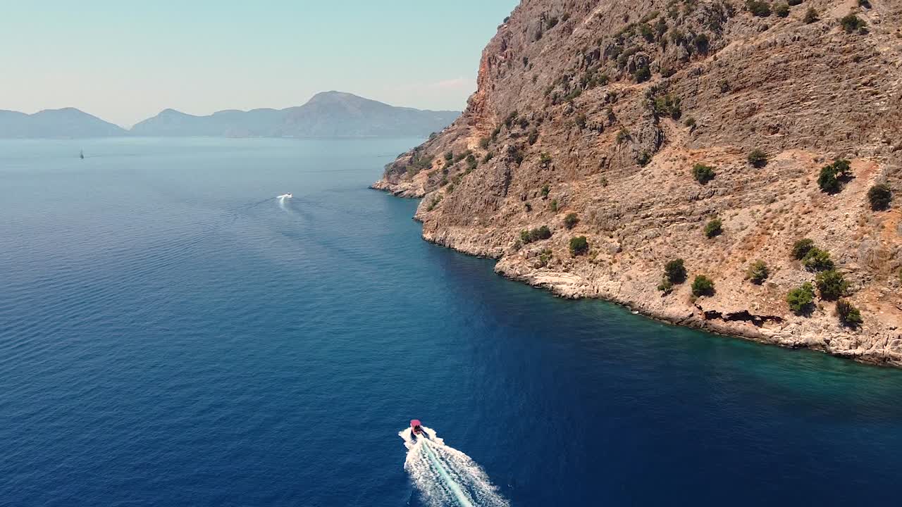 Aerial dolly shot following small boat in beautiful blue waters close to a rocky mountain